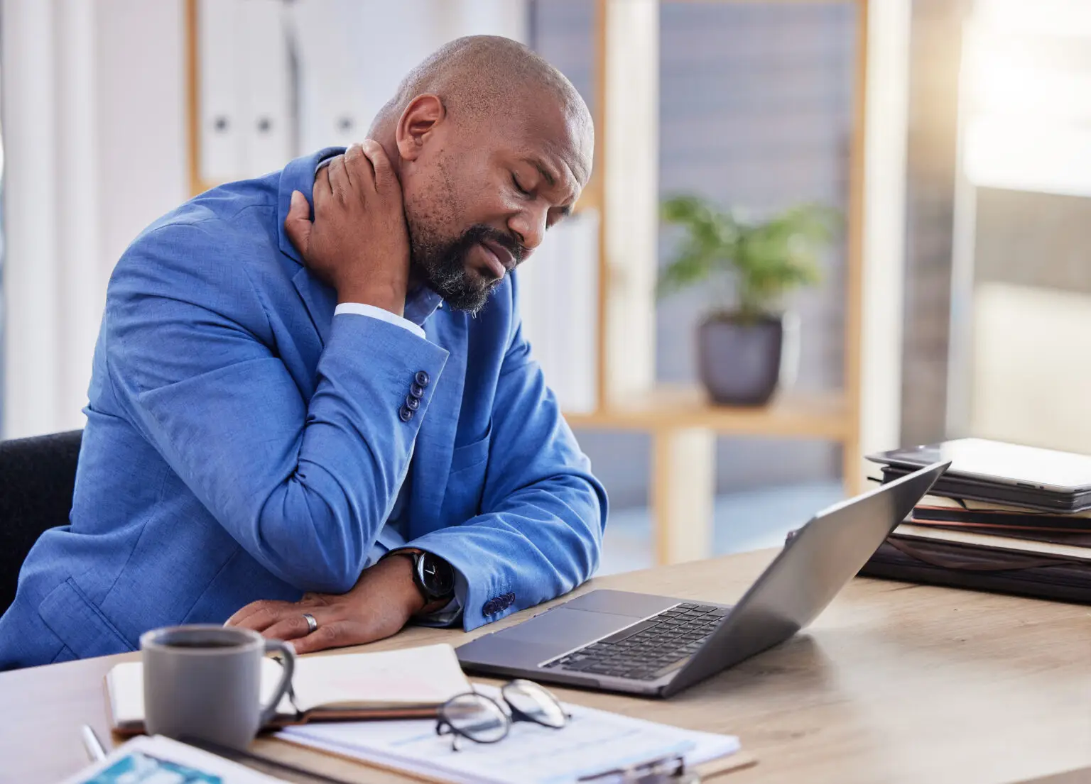 A man at a desk holding his neck in pain